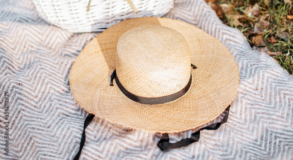 Straw hat on a plaid in the garden on the grass. Picnic in summer or spring.