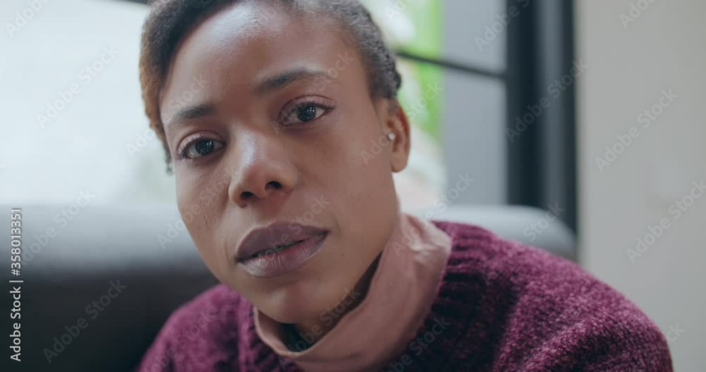 closeup and moving shoot of a young african woman sitting on the couch staring the camera a lady looking at the shot with no expression  on sofa at home