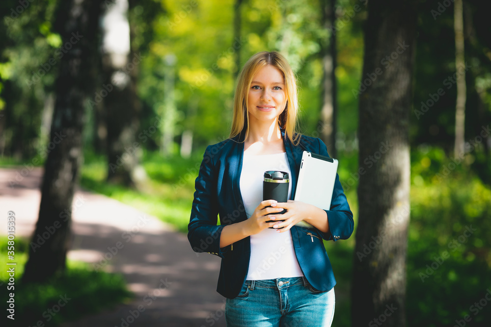 Young happy smiling caucasian adult girl business student walking outdoor concept in the park holding reading tablet thinking of credit finance job in the college with wireless headphones drink coffee Young happy smiling caucasian adult girl business student walking outdoor concept in the park holding reading tablet thinking of credit finance job in the college with wireless headphones drink coffee