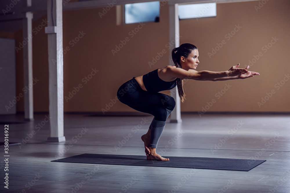 Fototapeta premium Young fit brunette standing in eagle yoga pose. Yoga studio interior.