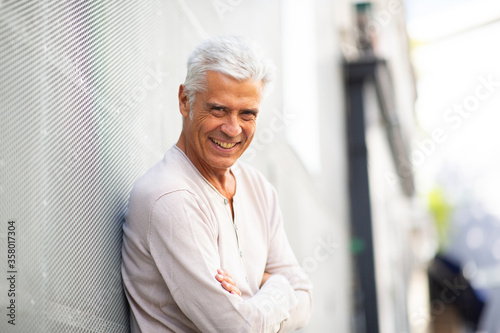 Side of handsome older man smiling with arms crossed outdoors