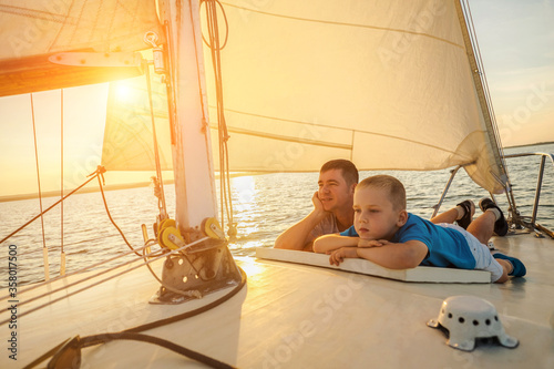 Happy traveler father and son enjoying sunset from deck of sailing boat moving in sea at evening time. Bonding Travel, Summer, Holidays, Journey, Trip, Lifestyle, Yachting concept © Andrii IURLOV