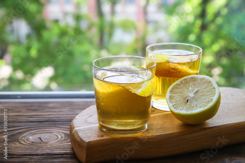 Cold kombucha with lemon in glasses on wooden background with copy space. Summer fermented raw tea