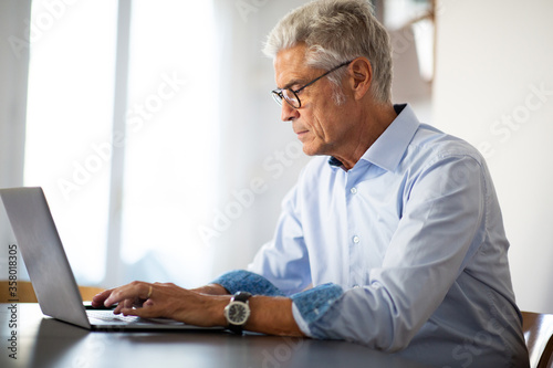 Side of businessman with glasses sitting at office desk using laptop comp[uter photo