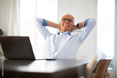 cheerful businessman relaxing in office with hands behind head