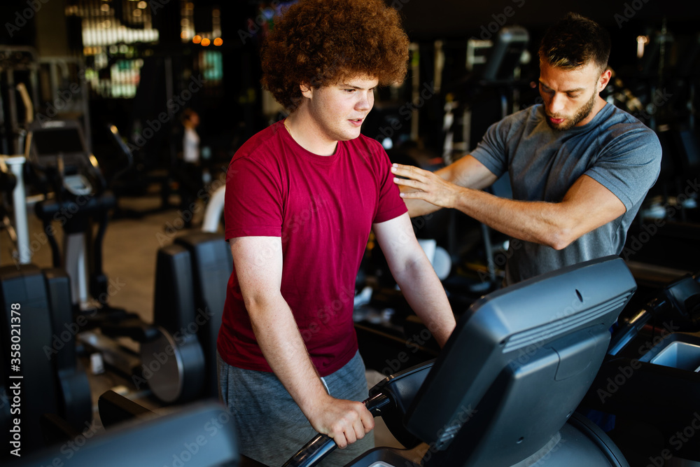 Overweight young man with trainer exercising in gym Overweight young man with trainer exercising in gym