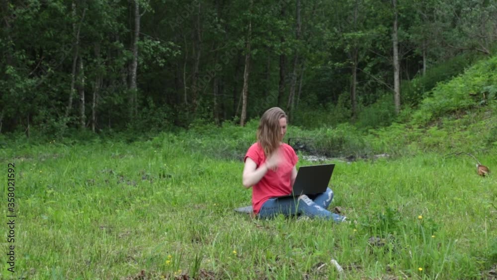 girl outdoors in the park working on a laptop, brushes off mosquito insects girl outdoors in the park working on a laptop, brushes off mosquito insects