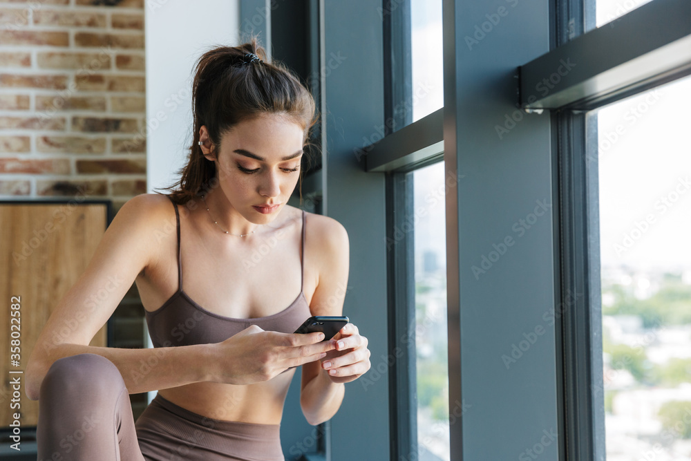 Image of young athletic woman using mobile phone while working out
