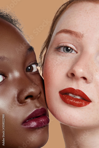 The real beauty exists in every corner of the world and is presented by women of all races. Beauty portrait of two ladies with different skin colour. Girls with rouged lips are posing cheek to cheek.  photo