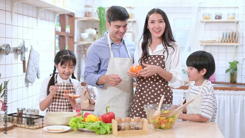 Happy family of Caucasian husband and Asian wife with their son and daughter cooking together in the kitchen happily.