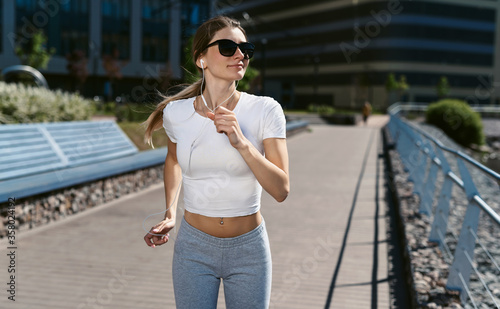 Young fitness woman runner running in the morning on the promenade or embankment and doing sports exercises. Healthy lifestyle  street training  social distancing