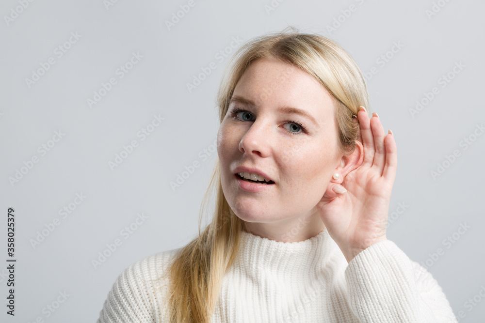 Young woman with hand at her ear tries to listen better Young woman with hand at her ear tries to listen better