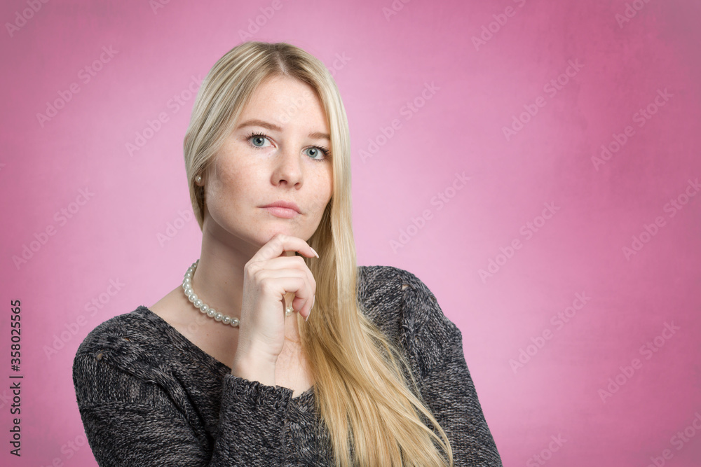 young doubtful woman with her hand at her chin in front of a pink background young doubtful woman with her hand at her chin in front of a pink background