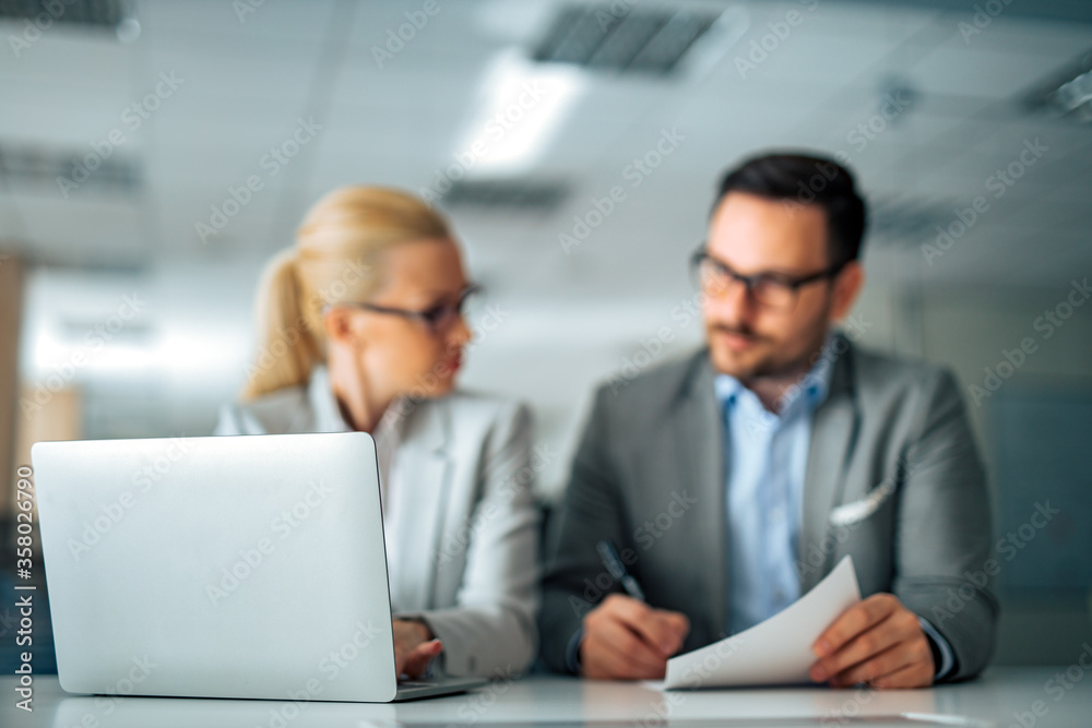 Business concept. Two business people sitting at desk with document and laptop, focus on laptop. Business concept. Two business people sitting at desk with document and laptop, focus on laptop.