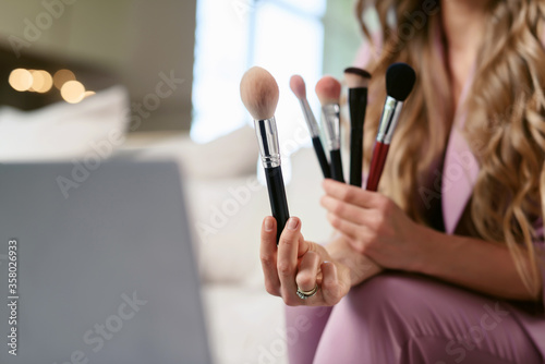 Attractive female make-up artist streaming on a laptop. Beauty blogger talking about various / different makeup brushes and shows them to her subscribers online