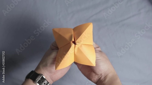 Close-up on Hands Playing with Orange Folded Paper Fortune Teller Origami photo