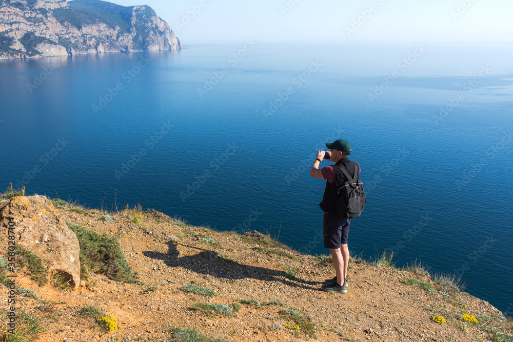A young traveller takes photos on his phone of a beautiful view of the sea