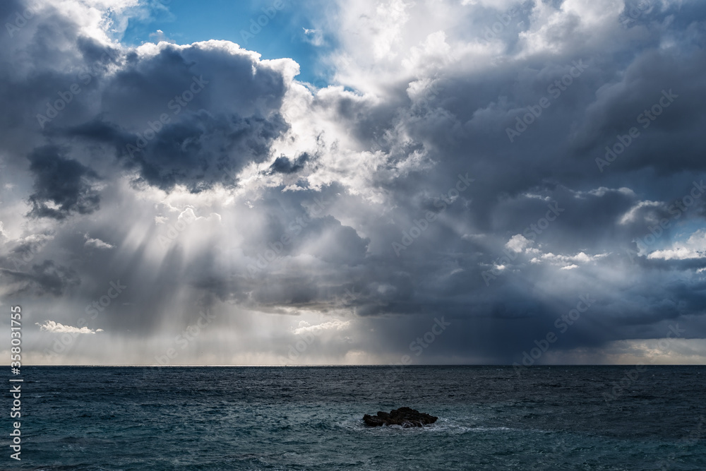 Obraz premium Sun rays through dark rain clouds over the sea