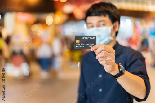 credit card with young asian man wearing medical mask at shopping mall for prevention from coronavirus (Covid-19) pandemic. new normal concepts