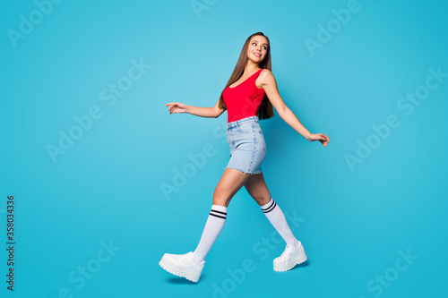 Fototapeta Naklejka Na Ścianę i Meble -  Full size profile side photo of cute lovely pretty content girl walk go enjoy spring free time weekend look copyspace wear legs shoes tank-top isolated over blue color background