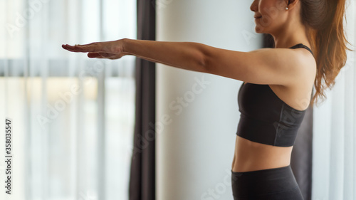 Closeup image of a young woman stretching arms to warm up before workout at home