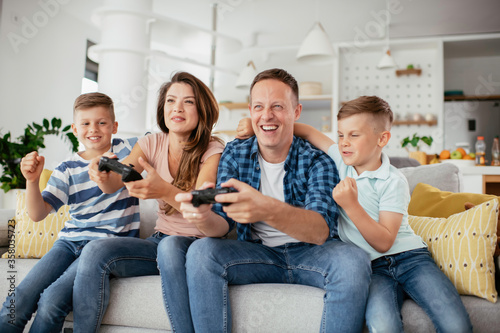 Husband and wife playing video games with joysticks in living room. Loving couple are playing video games with kids at home.