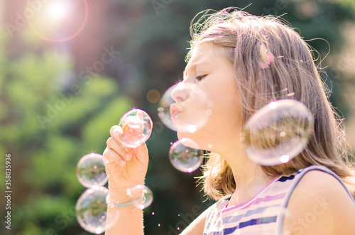 little girl blowing bubbles at park in a sunny days