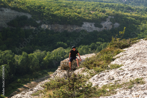 A young man is sitting on the edge of a cliff. The concept of mountaineering and tourism