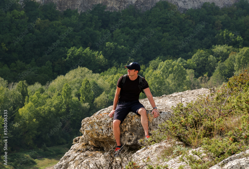 A young man is sitting on the edge of a cliff. The concept of mountaineering and tourism