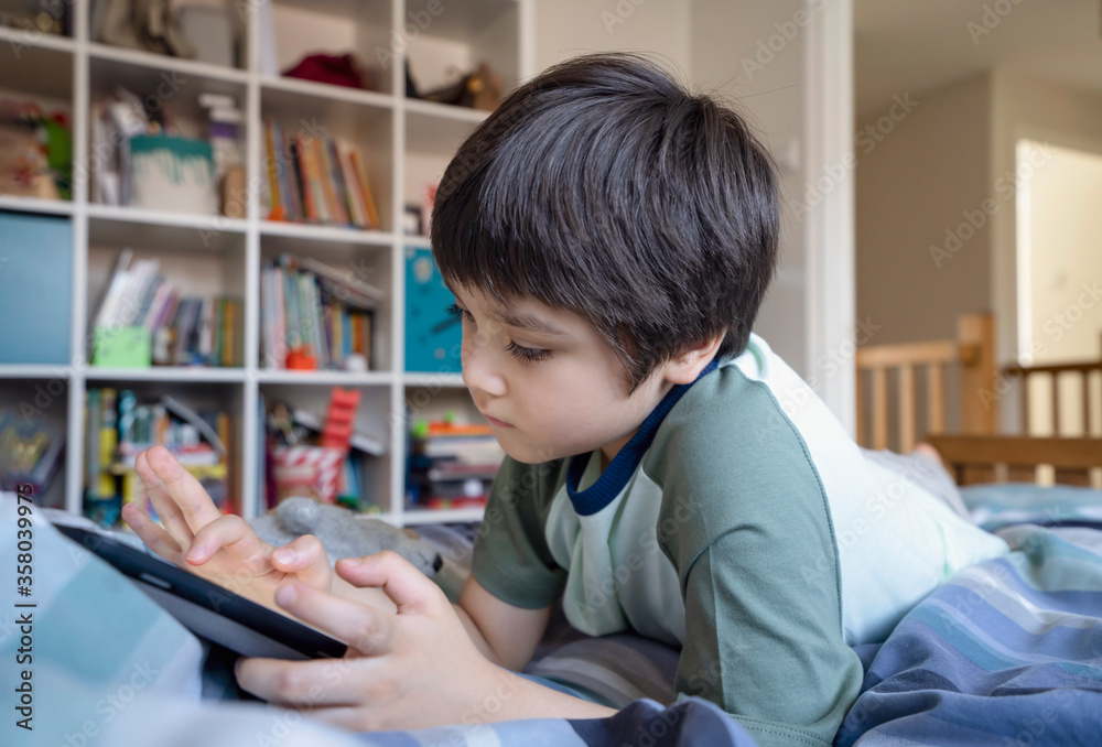 Kid using tablet for his homework, Child lying in bed using digital tablet searching information on internet,Home schooling, online education Kid using tablet for his homework, Child lying in bed using digital tablet searching information on internet,Home schooling, online education
