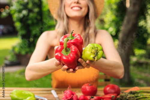 Young pretty girl in a hat is sitting at wooden table with fresh vegetables grown in her garden in the summer. close up