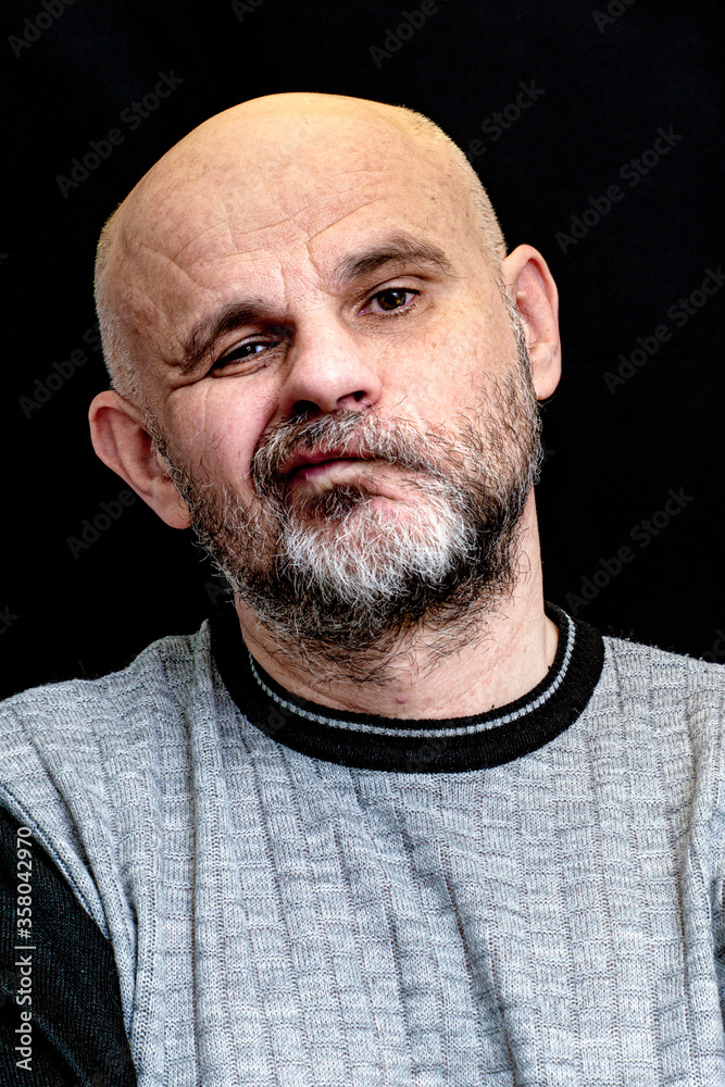 portrait of a middle-aged bald bearded man on a black background with the silly grin on his face portrait of a middle-aged bald bearded man on a black background with the silly grin on his face