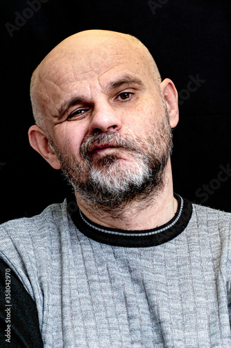 portrait of a middle-aged bald bearded man on a black background with the silly grin on his face