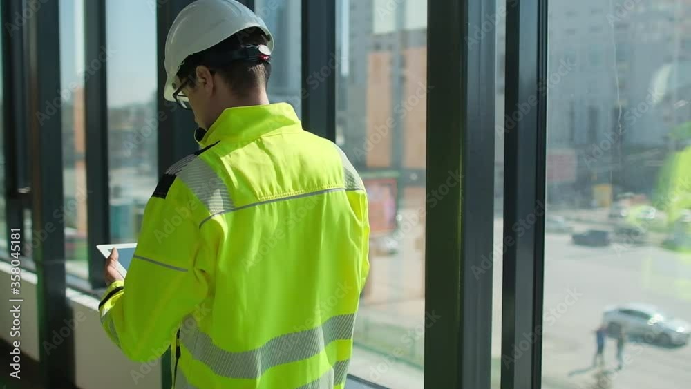 Male builder engineer man worker foreman architect in hard hat with tablet computer working walking browsing building project indoor of window construction site. Industrial building. engineering. 4 k