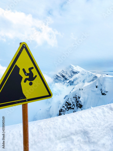 Sign attention in the foreground. Do not fall. Against the backdrop of snowy mountains, blue sky with clouds