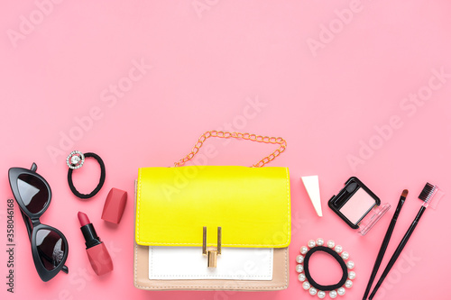 Fototapeta Naklejka Na Ścianę i Meble -  Yellow handbag with woman's accessories. Sunglasses, lipstick, blush, scrunchy, brushes isolated on pink background Top view Flat lay Beauty, fashion, party, shopping concept