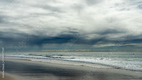 Surf waves breaking on a sandy beach, with heavy grey clouds over the sea and rain showers on the horizon. Currumbin Beach, Gold Coast, Queensland, Australia.