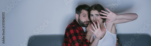 scared girl with outstretched hands watching movie near frightened boyfriend, horizontal image