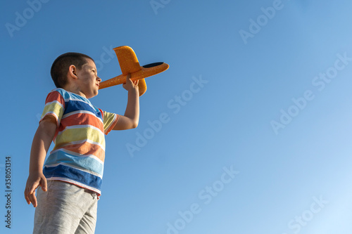Boy launches the plane, raising arms over blue sky at summer. Dreams, freedom and  concept of travel.  Copy space.