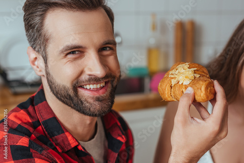cropped view of girl near happy man holding croissant and looking at camera