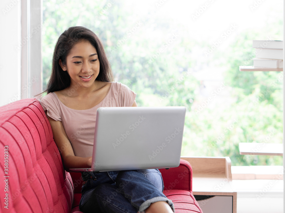 Young asian teen use laptop computer on the red sofa to relax in the living room Young asian teen use laptop computer on the red sofa to relax in the living room