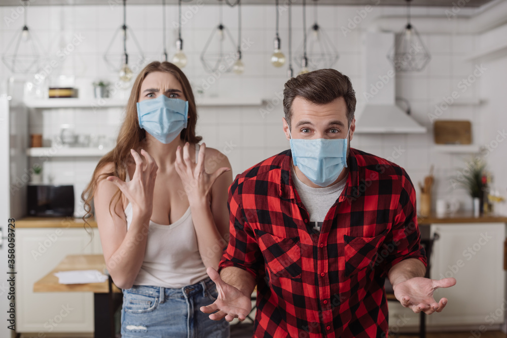 irritated couple in medical masks screaming and gesturing while looking at camera