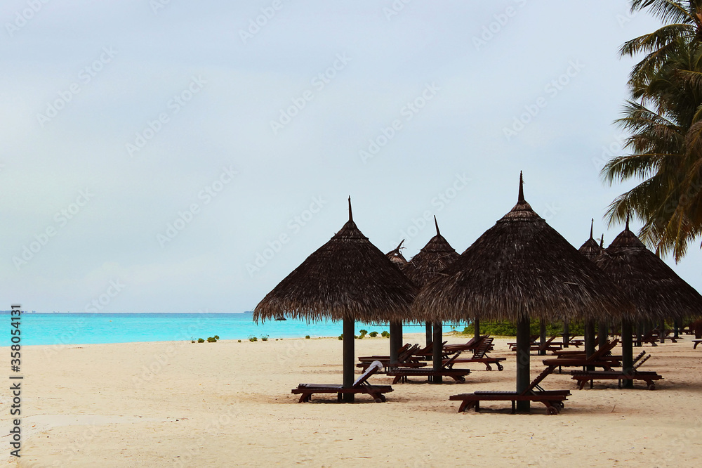 Sunbeds and umbrellas in the shade of the palm trees, Maldives islands. Luxury resort in Indian ocean. Tropical beach vacation in exotic place, travel concept