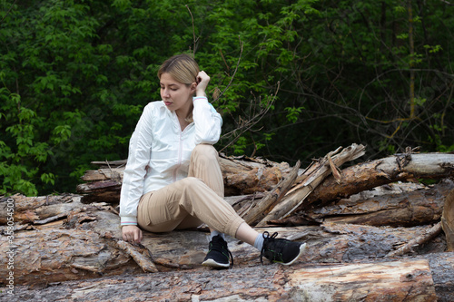 Outdoor close up portrait of young beautiful woman coat,sitting on a tree stump, Trees Chopped And Stacked In Forest