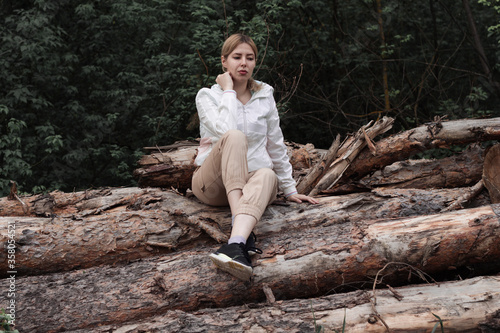 Outdoor close up portrait of young beautiful woman coat,sitting on a tree stump, Trees Chopped And Stacked In Forest