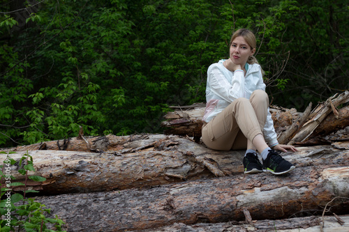 Outdoor close up portrait of young beautiful woman coat,sitting on a tree stump, Trees Chopped And Stacked In Forest