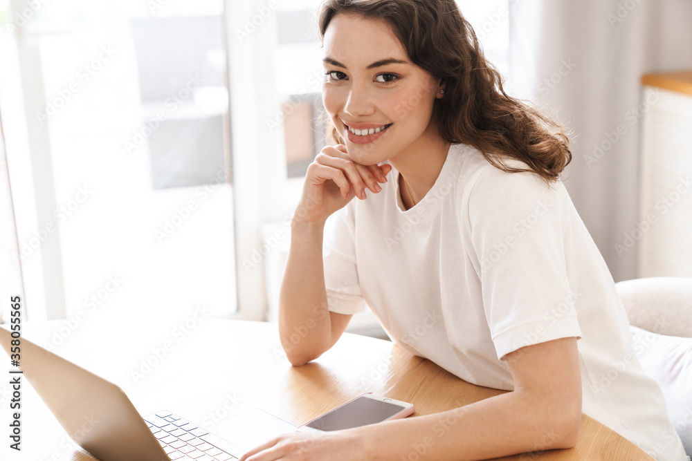 Photo of woman using laptop and cellphone while sitting at kitchen Photo of woman using laptop and cellphone while sitting at kitchen