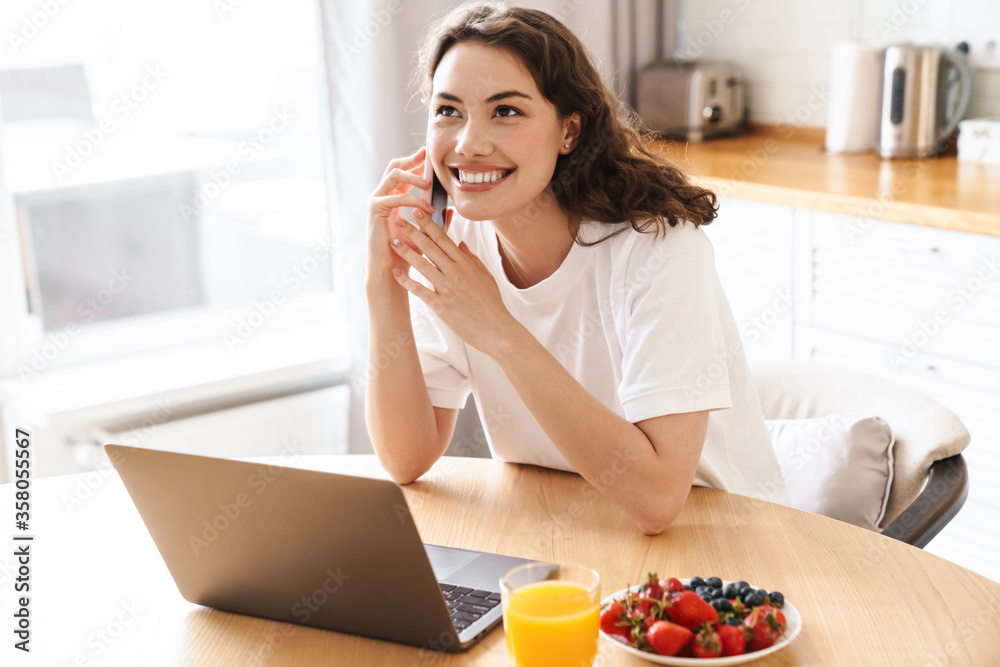 Photo of smiling beautiful woman using laptop and talking on cellphone