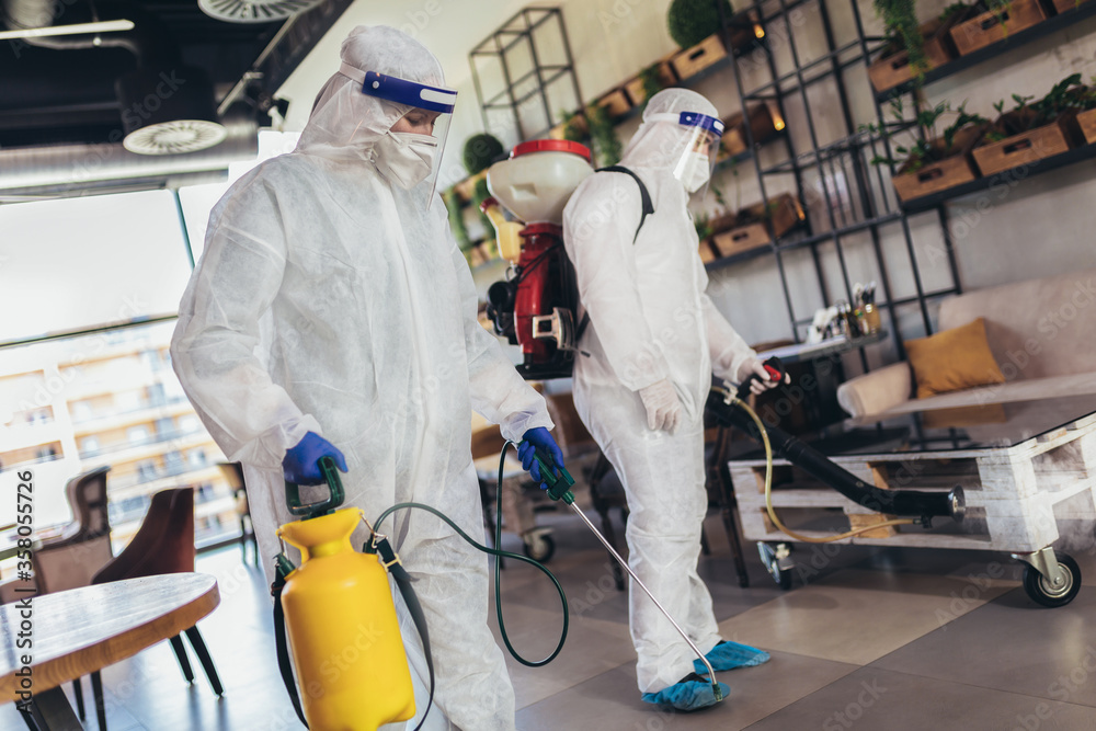 Professional workers in hazmat suits disinfecting indoor of cafe or restaurant, pandemic health risk, coronavirus