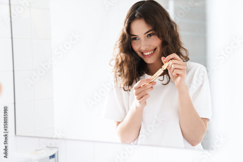 Photo of woman smiling and holding mascara while looking at mirror